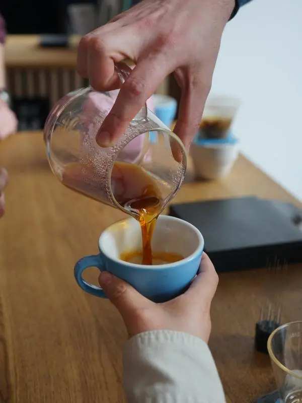 The Coffee Collective - hand poring coffee from a mug into a cup